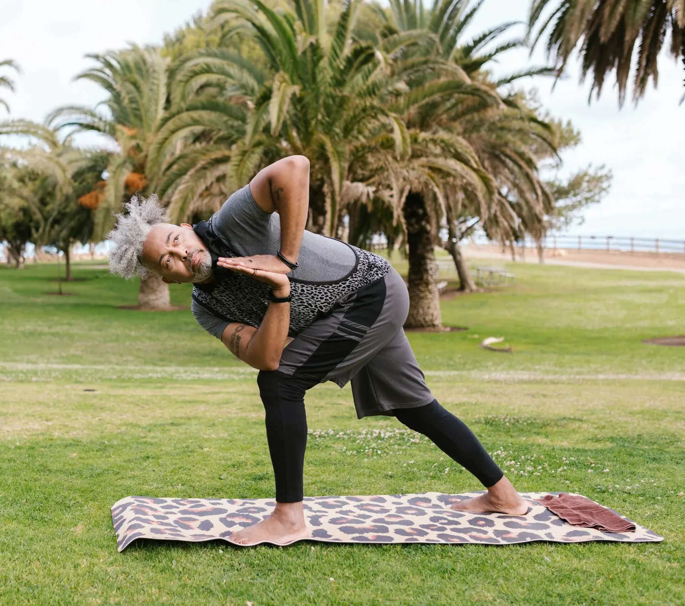 A man doing a yoga pose in a park by the water